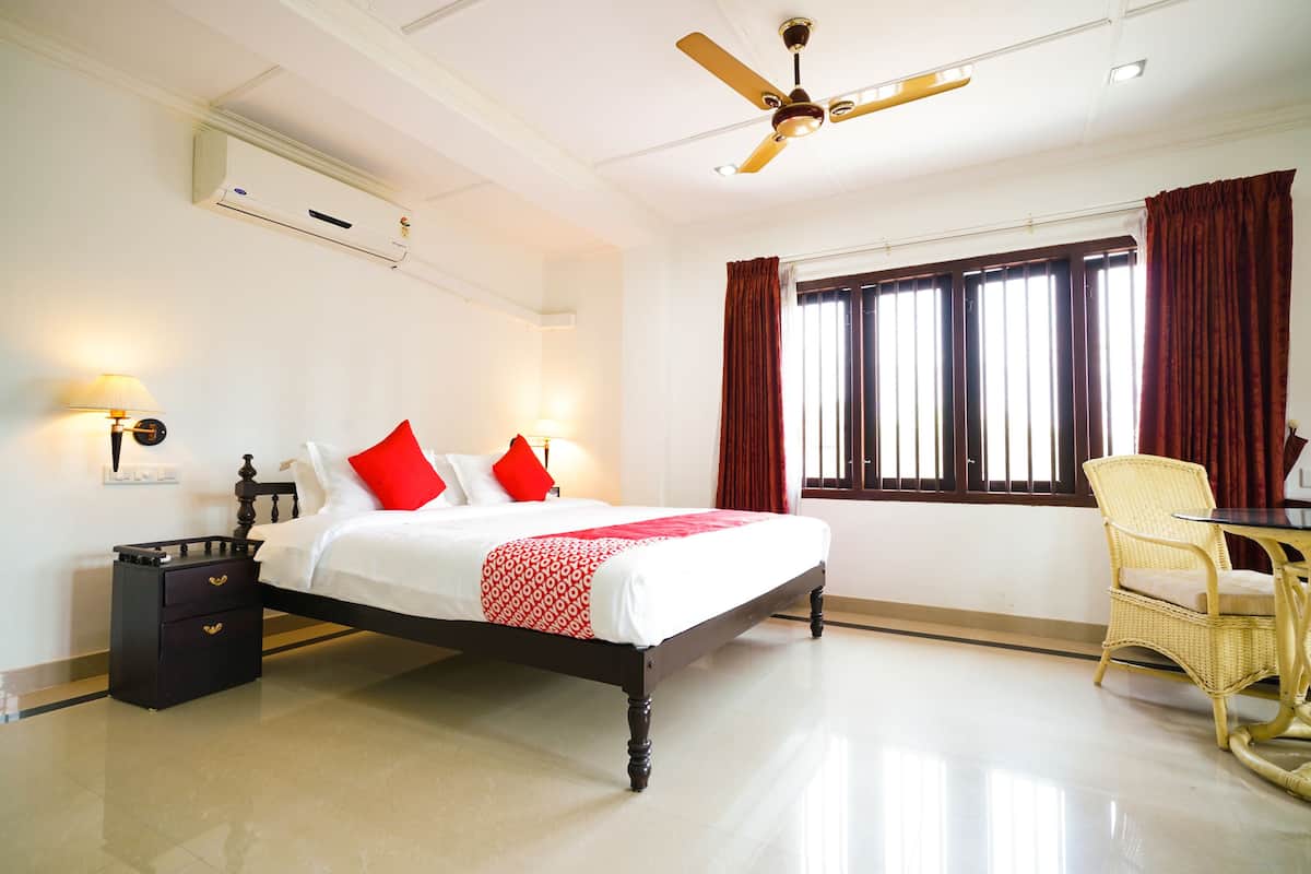 Habitación de hotel con cama, mesitas de noche, escritorio, silla, ventilador de techo y ventana con cortinas.