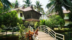 A traditional house with a tiled roof, surrounded by lush greenery and palm trees. - Palette Resorts- Tapovan Green County (Kothamangalam)