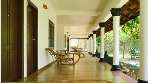 A covered corridor with wooden flooring, white columns, and a bench. - Palette Resorts- Tapovan Green County (Kothamangalam)