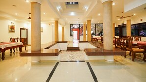 A spacious lobby with a central marble staircase, wooden chairs, and tables arranged for dining. - Palette Resorts- Tapovan Green County (Kothamangalam)