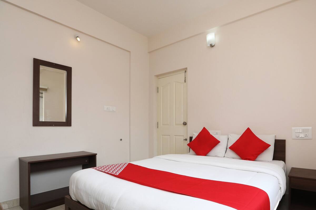 A hotel room with a bed, a bedside table, a dresser, a mirror, and a door.