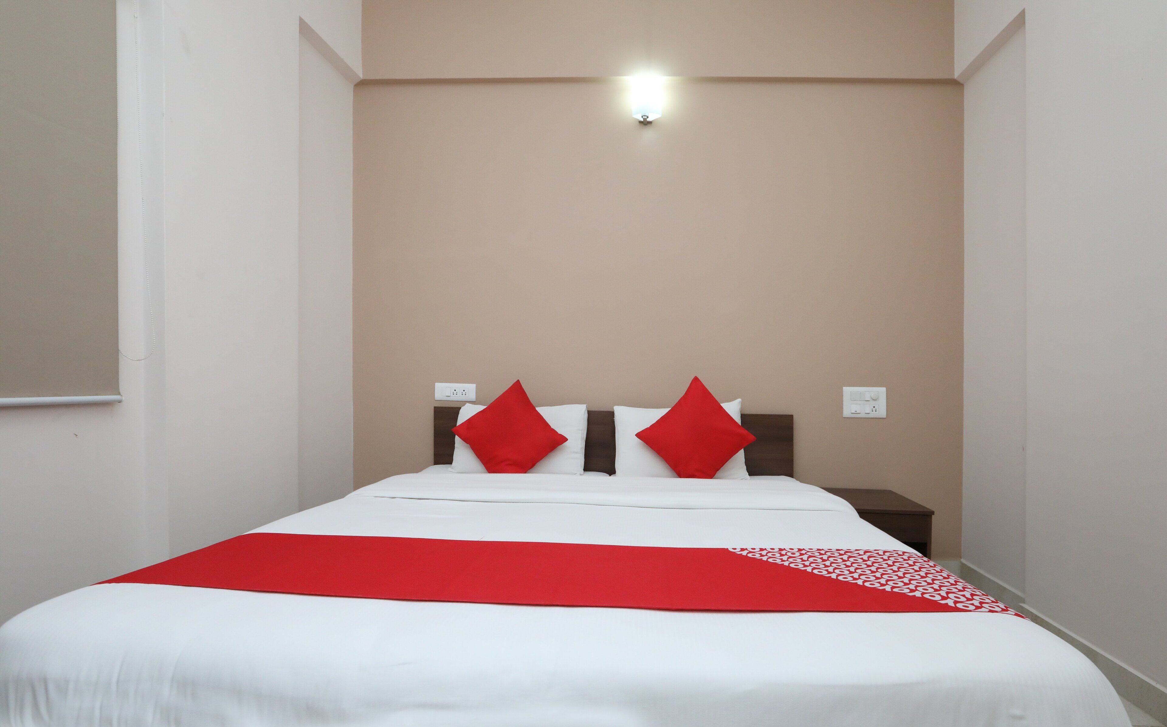 A hotel room with a bed, a nightstand, and a wall-mounted light fixture.
