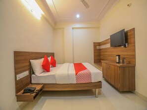 Une chambre d’hôtel moderne avec un lit en bois, des oreillers rouges, une télévision et une petite table d’appoint en bois sur laquelle se trouve un téléphone.