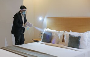 A person using a spray device in a hotel room with a bed, pillows, and a nightstand. - OYO Flagship 28149 Mangal Residency (Udaipur)
