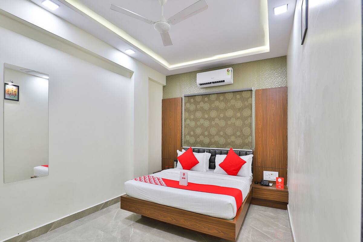 A modern hotel room with a wooden bed, red pillows, a ceiling fan, and an air conditioning unit.