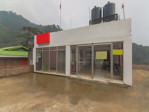 A modern building with large glass doors and windows, a red section on the roof, and water tanks on top.