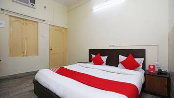 Habitación de hotel con cama, mesita de noche, cabecera de madera, colcha roja y blanca, y armario de madera.
