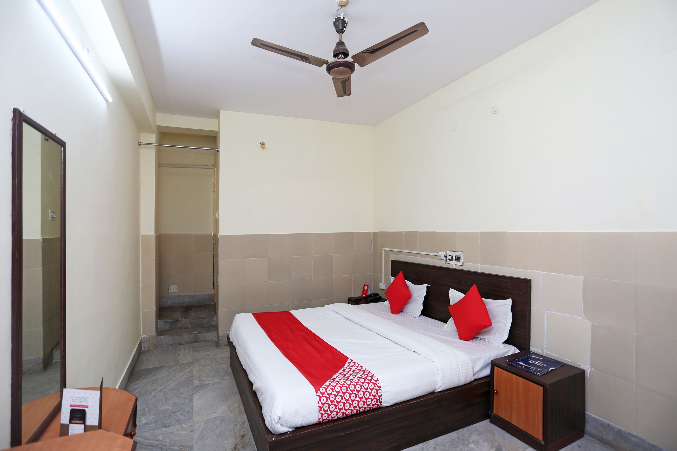 Ein Hotelzimmer mit Bett, Nachttisch, Deckenventilator und einem Badezimmer mit Dusche und Toilette.
