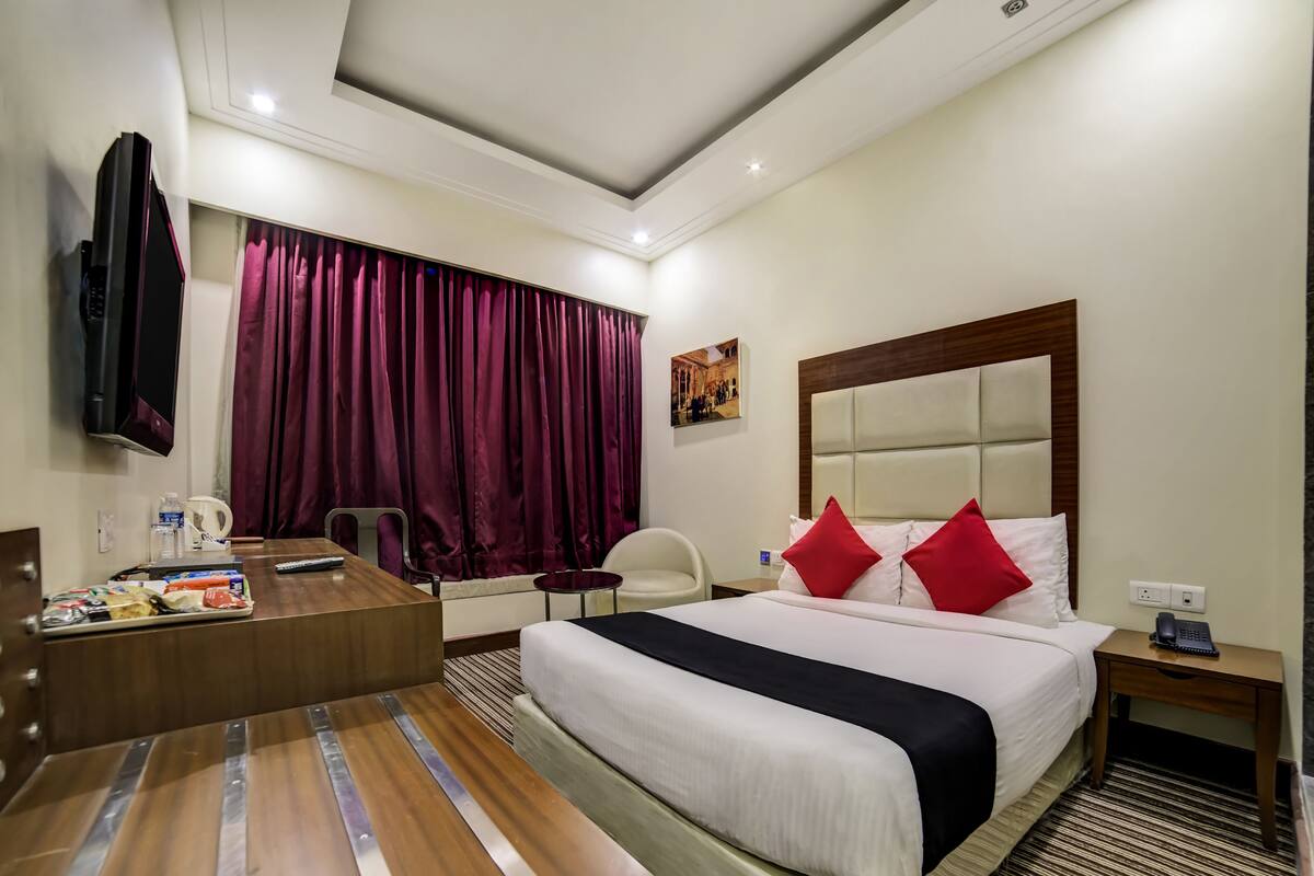 Habitación de hotel con cama, mesita de noche, escritorio, silla y televisor montado en la pared.