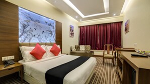 A hotel room with a bed, a desk, a chair, a sofa, a window with a tree mural, and a curtain. - Capital O 28618 New Haven Hotel (New Delhi)