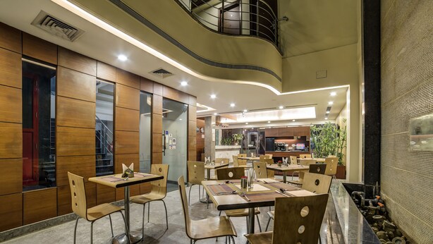 A modern dining area with wooden panel walls, metal chairs, and tables. - Capital O 28618 New Haven Hotel (New Delhi)
