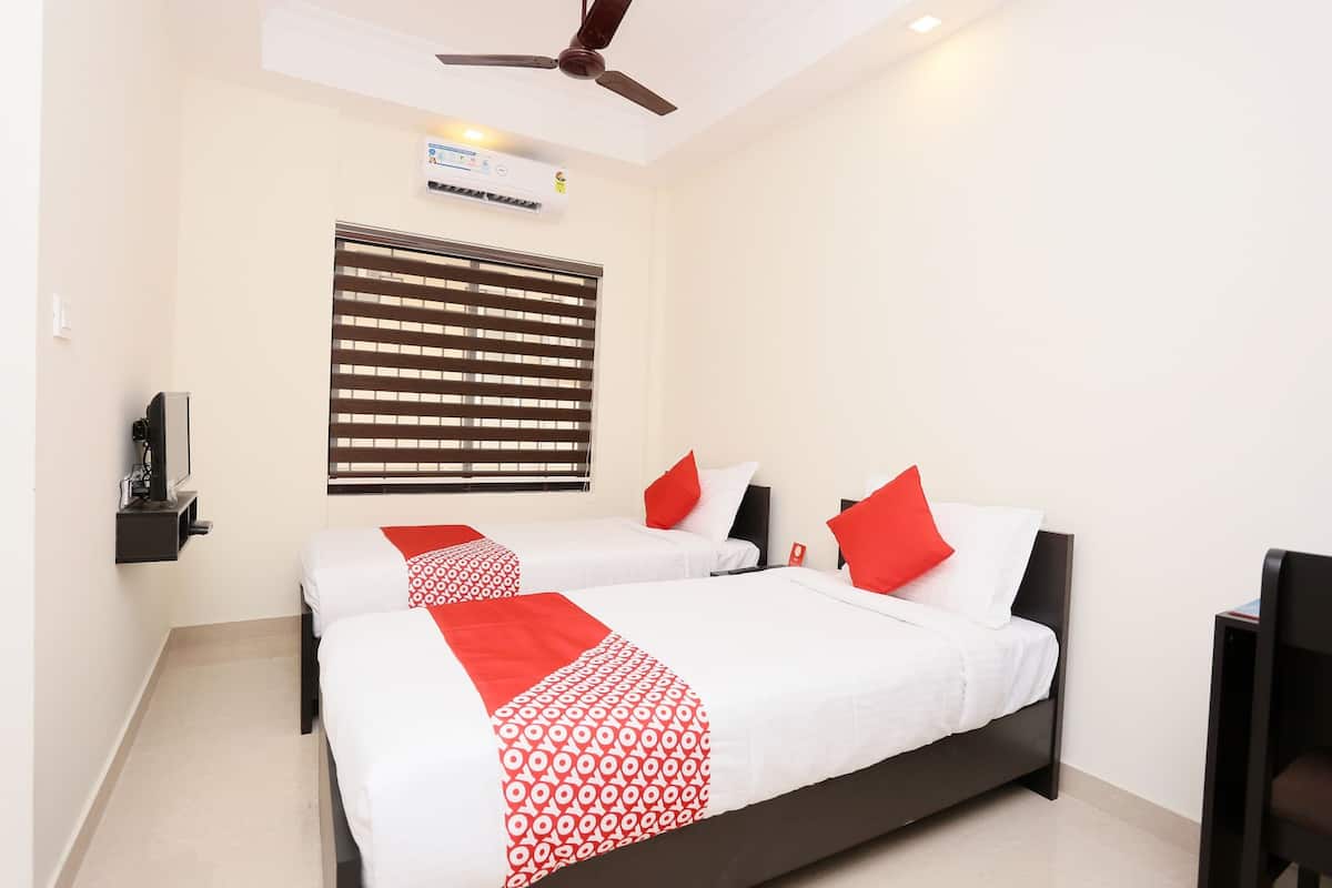 A hotel room with two beds, a ceiling fan, an air conditioning unit, a window with blinds, and a small table with a chair.