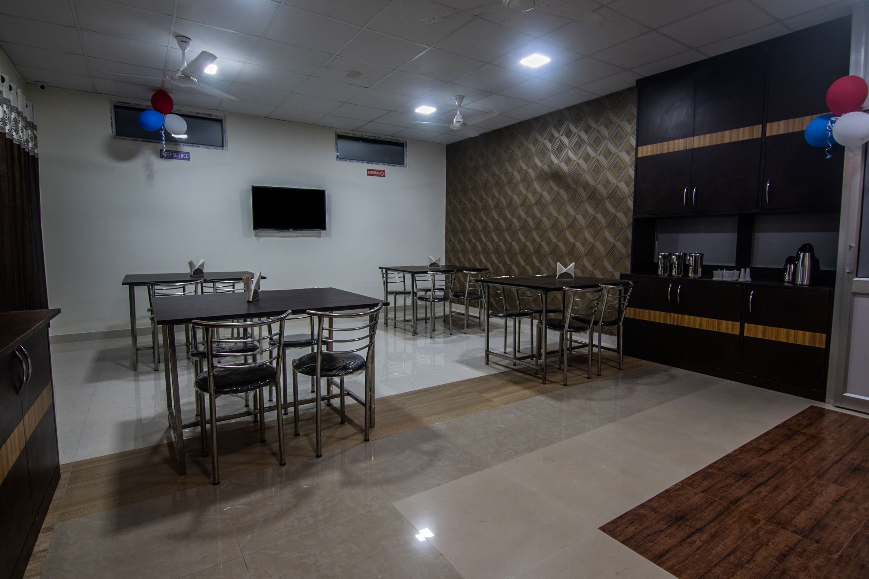 Sala de conferências com mesas, cadeiras, uma TV de tela plana e parede com padrão.