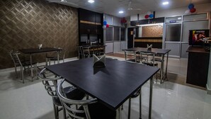 A dining area with a large table and chairs, a kitchen area, and a Nescafé display. - OYO 15700 Spectrum Residency (Guwahati)