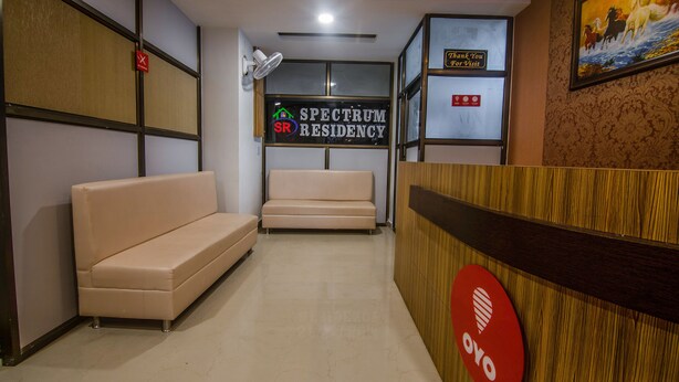 A reception area with a sofa, a wooden reception desk, and a sign that reads "SPECTRUM RESIDENCY". - OYO 15700 Spectrum Residency (Guwahati)