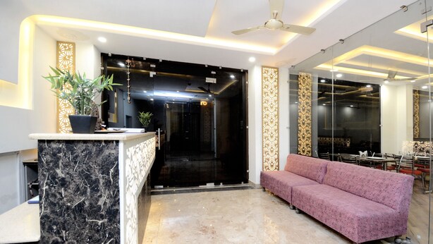 A modern reception area with a marble reception desk, a pink sofa, and a glass partition. - OYO 27061 Hotel Magnum (Mohali)