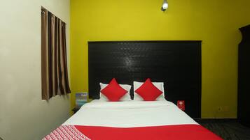 A hotel room with a bed, a headboard, a red and white bedspread, and a yellow wall.