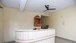 A room with a reception desk, a ceiling fan, a small wooden shelf, and a power outlet on the wall.