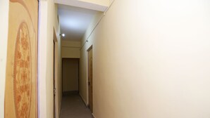 A narrow hallway with plain walls and doors, leading to a room with a visible door at the end.