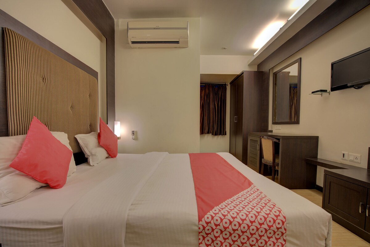 A hotel room with a bed, a desk, a chair, a wardrobe, and a TV.