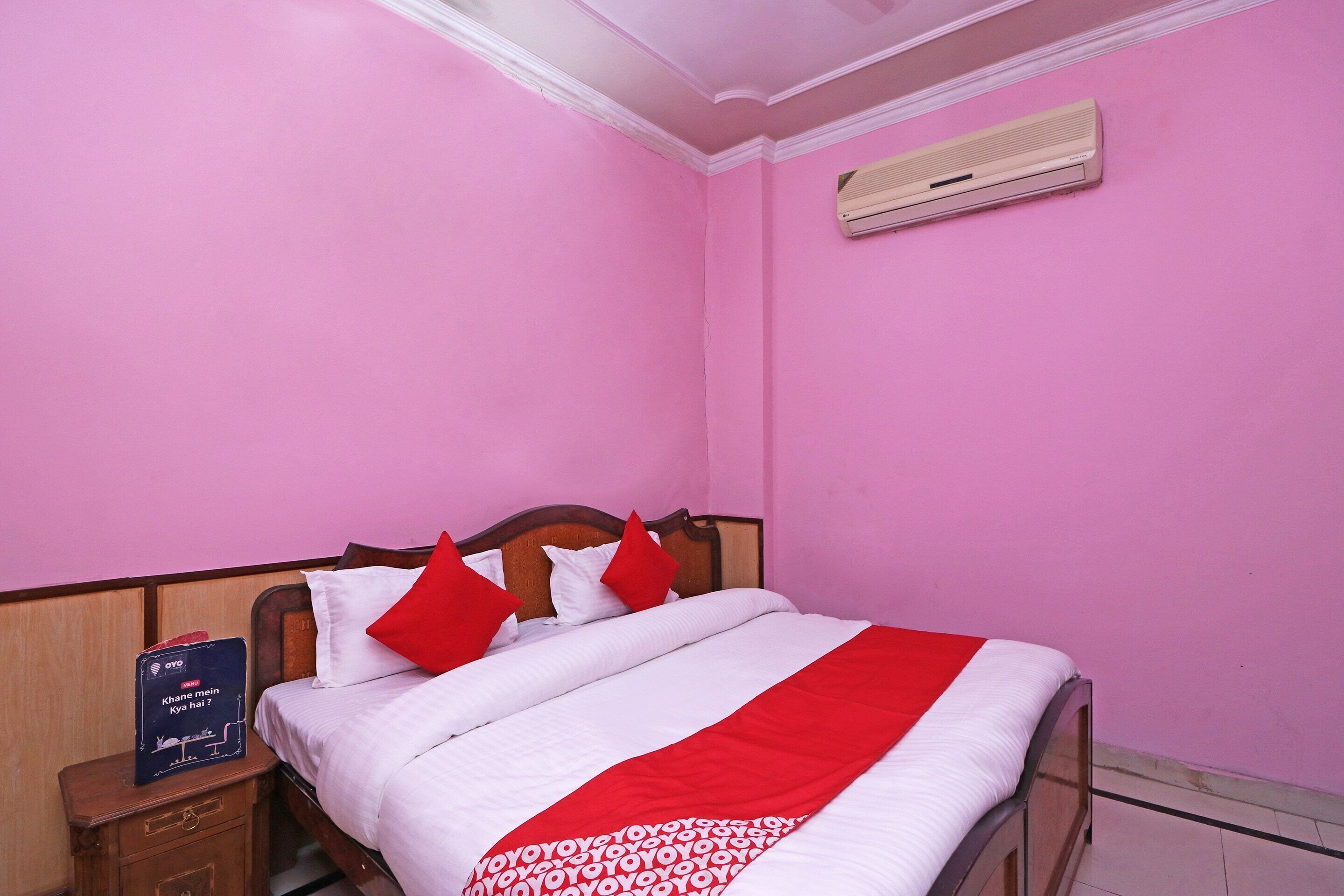 A bedroom with pink walls, a wooden bed frame, white bedding, and a red and white striped blanket.