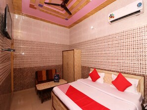 A hotel room with a bed, a wooden wardrobe, a small table with a book, and a ceiling fan. - OYO 22646 Jyoti Hotel (Rewari)