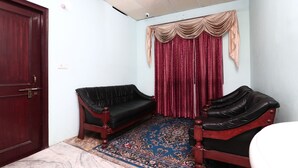 Una habitación con una puerta marrón oscuro, dos sofás de cuero negro, una alfombra estampada y una cortina roja con un frente beige.