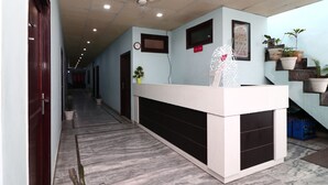 Un área de recepción con suelo de mármol, mostrador de recepción, plantas en macetas y un reloj en la pared.