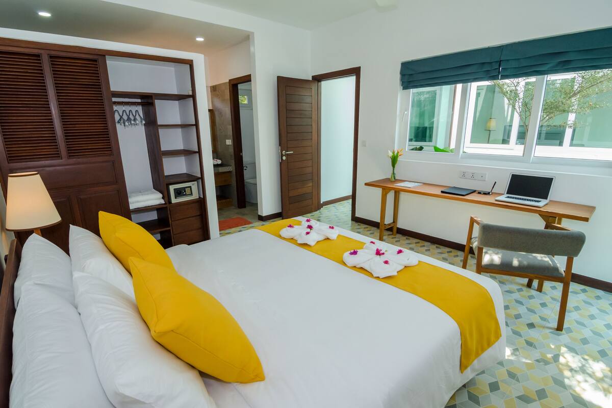A hotel room with a bed, a desk with a laptop, a chair, and a window with a view.