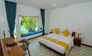 A hotel room with a bed, bedside lamps, a desk with a chair, a window with curtains, and a view of a pool. - Draco Residence (Siem Reap)