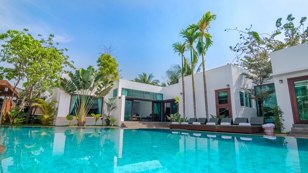 A modern pool area with clear blue water, surrounded by lush greenery and contemporary architecture. - Draco Residence (Siem Reap)