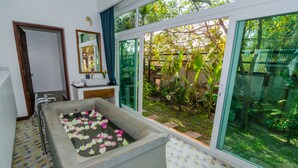A bathroom with a large bathtub filled with water and floating flowers, a sink, and a mirror. - Draco Residence (Siem Reap)
