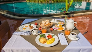 A breakfast setup with eggs, toast, fruit, and coffee by a poolside. - Draco Residence (Siem Reap)
