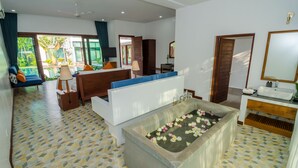 A modern hotel room with a large bathtub, a sofa, a TV, and a balcony with plants. - Draco Residence (Siem Reap)