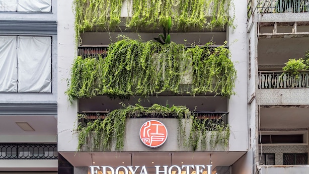 The EDOYA HOTEL entrance with a modern design, including a sign with a red and white logo, a glass facade, and a parking area with scooters. - Edoya Hotel Ben Thanh (Ho Chi Minh City)