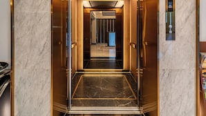 An elevator with marble walls and a metallic finish, leading to a hallway with a modern design and a digital display. - Edoya Hotel Ben Thanh (Ho Chi Minh City)