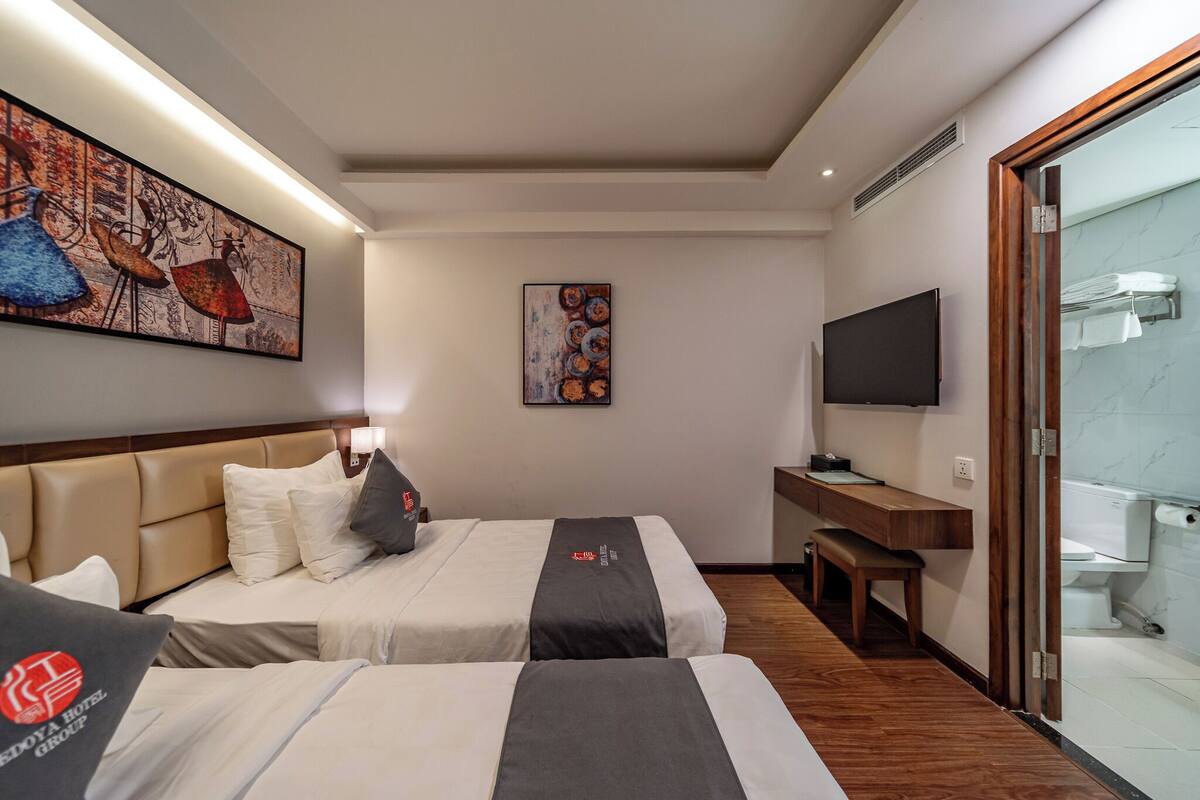 Ein Hotelzimmer mit zwei Betten, einem Schreibtisch, einem Fernseher und Bildern an den Wänden.