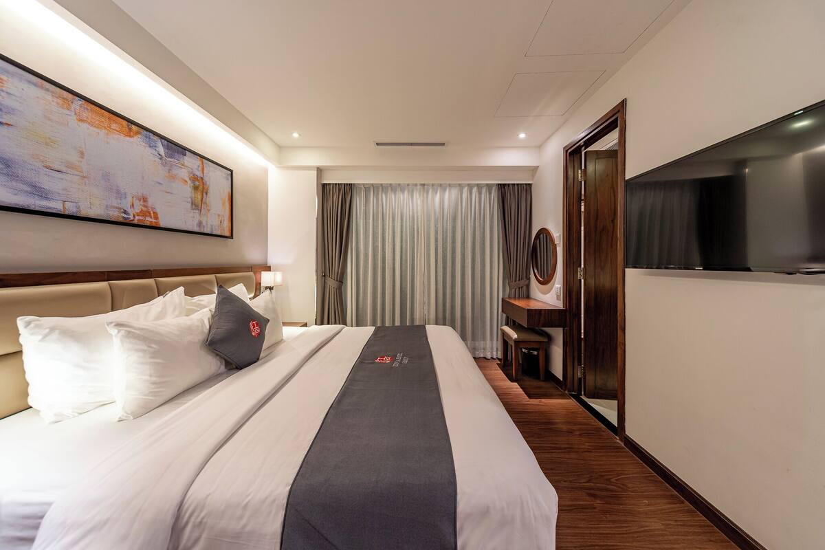 Ein Hotelzimmer mit einem großen Bett, einem Flachbildfernseher, einem Schreibtisch und einem großen abstrakten Gemälde an der Wand.