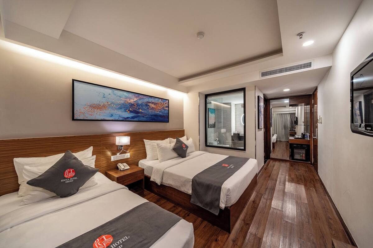 Ein Hotelzimmer mit zwei Betten, einem großen Gemälde an der Wand, einem Spiegel und Blick ins Bad.