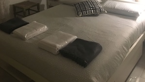 Une chambre à coucher avec un lit, des oreillers, une couverture, une table de chevet, une lampe, une décoration murale et un tableau encadré.