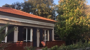 Un bâtiment à deux étages, avec un toit recouvert de tuiles rouges, un balcon doté d’une balustrade en bois et un grand arbre sur la droite.
