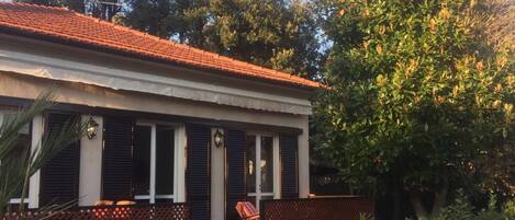 A two-story building with a red-tiled roof, a balcony with a wooden railing, and a large tree to the right.