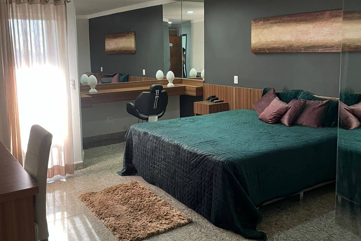 A modern hotel room with a bed, a desk, a chair, a mirror, and a rug.