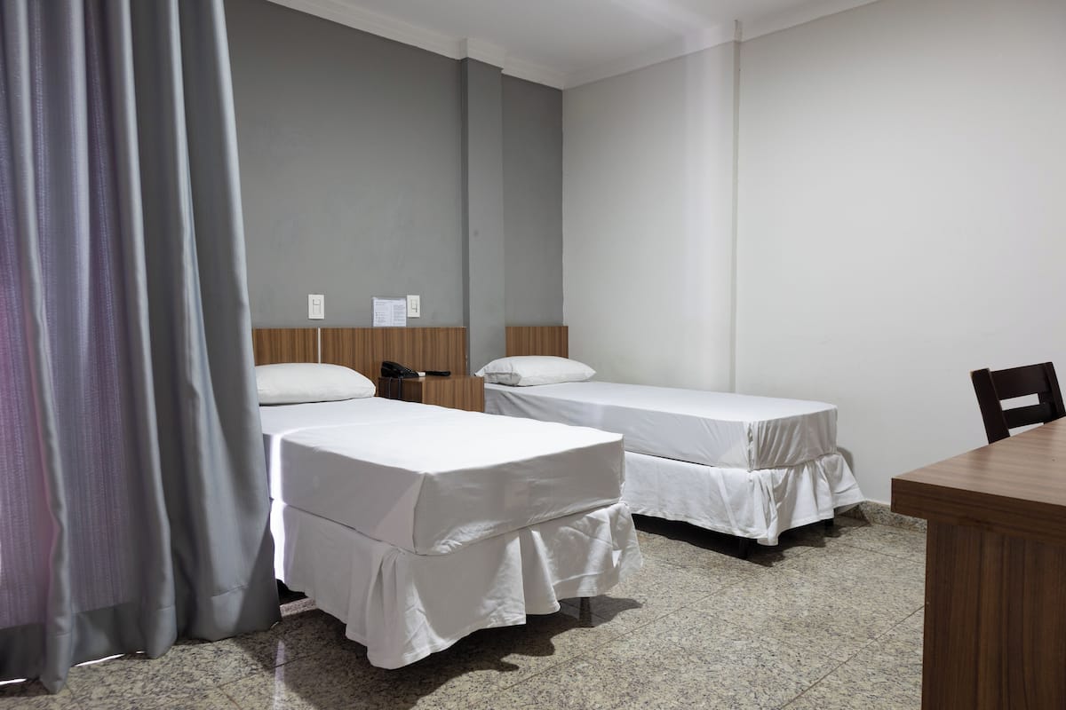 A hotel room with two beds, a wooden table, and a curtain.