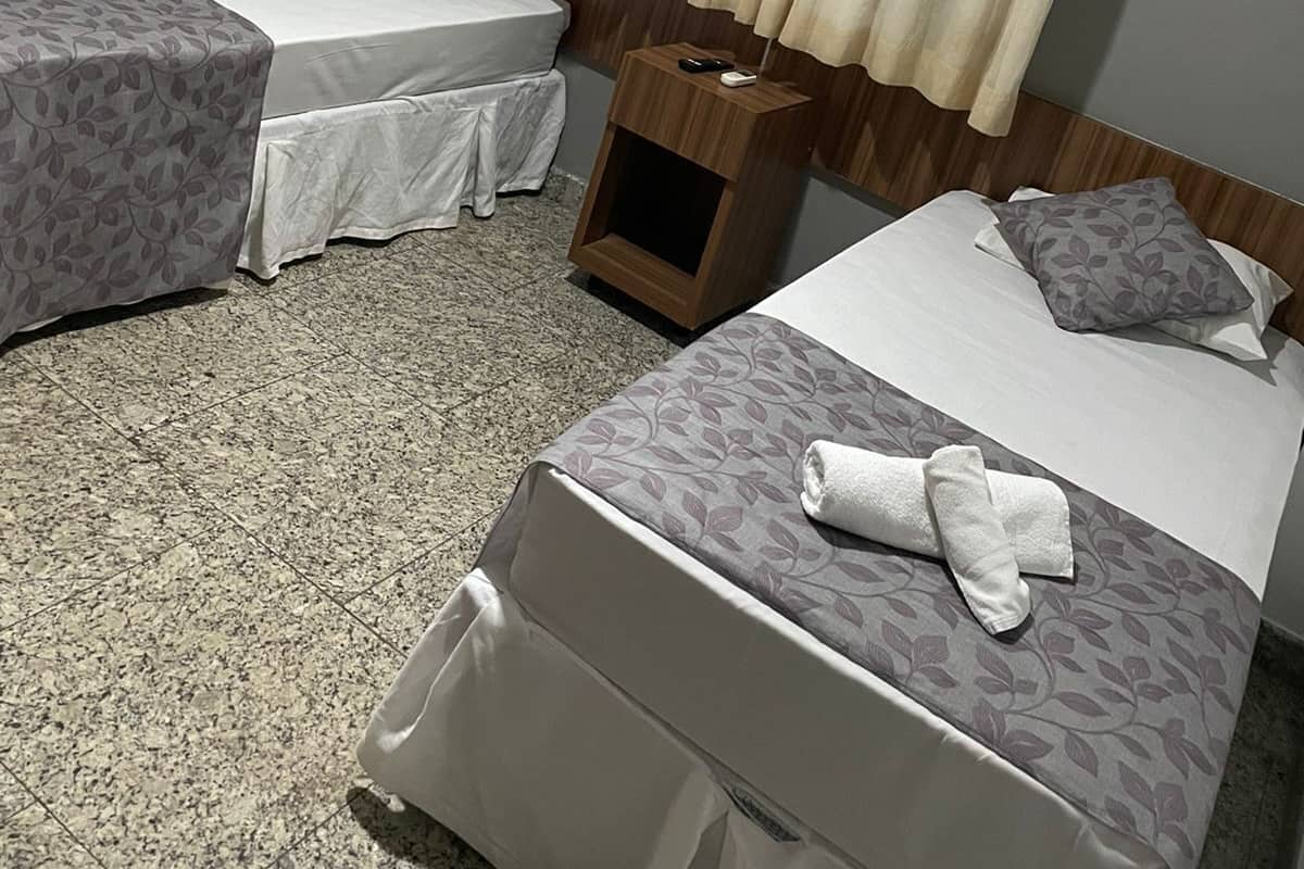 A hotel room with two single beds, a wooden headboard, a nightstand, and a curtain.