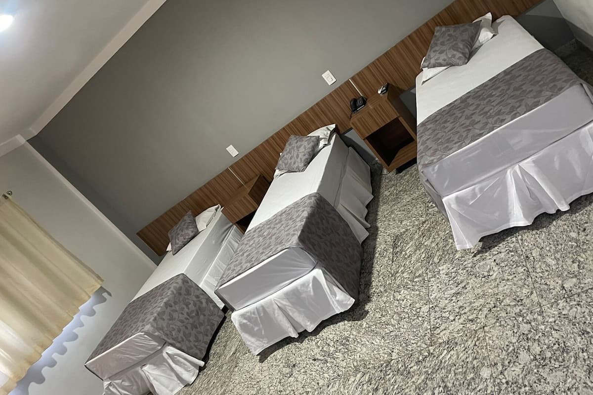 A hotel room with three beds, a wooden headboard, a carpeted floor, and a small bedside table with a lamp.