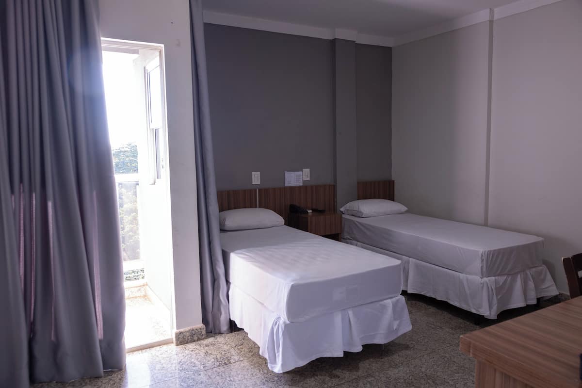 A hotel room with two single beds, a wooden nightstand, a desk, and a chair.