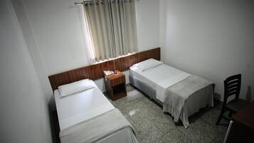 Een kleine, schone kamer met twee eenpersoonsbedden, een houten nachtkastje, een tafeltje en een stoel.