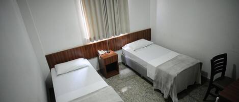 Ein kleines, sauberes Zimmer mit zwei Einzelbetten, einem Holznachttisch, einem kleinen Tisch und einem Stuhl.
