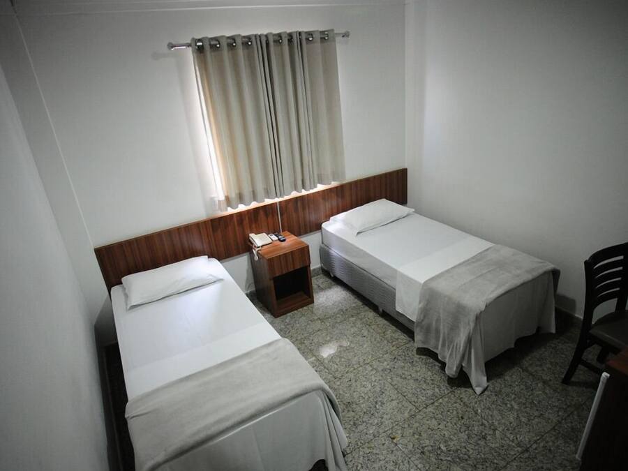 Een kleine, schone kamer met twee eenpersoonsbedden, een houten nachtkastje, een tafeltje en een stoel.